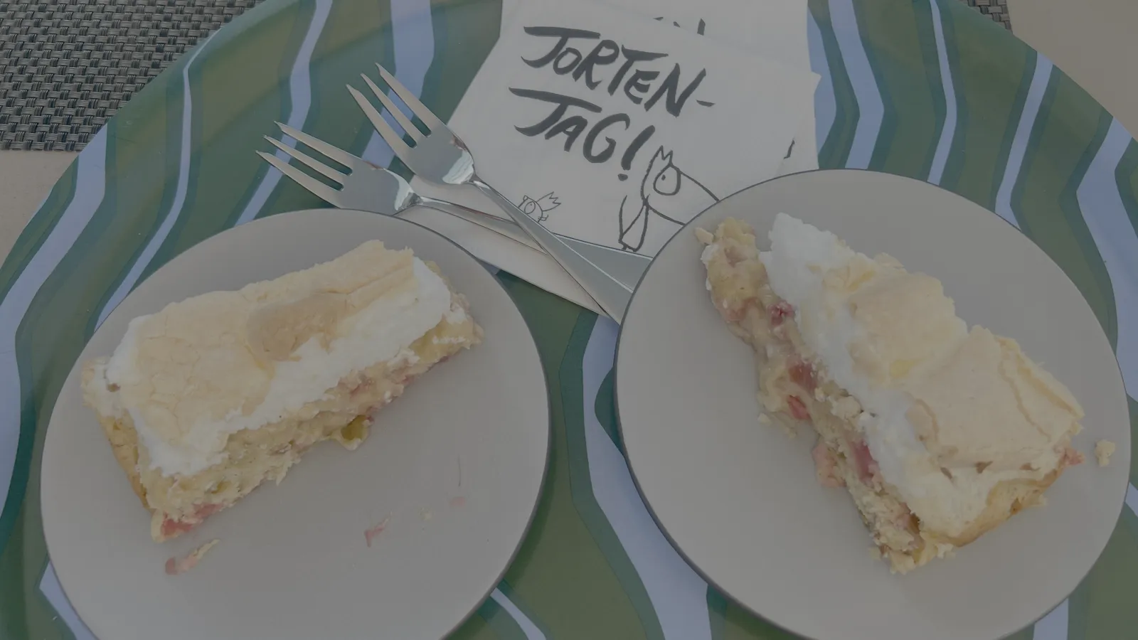 Zwei Kuchenstücke auf dem Gartentisch, daneben ein Zettel mit der Aufschrift „Torten-Tag!“